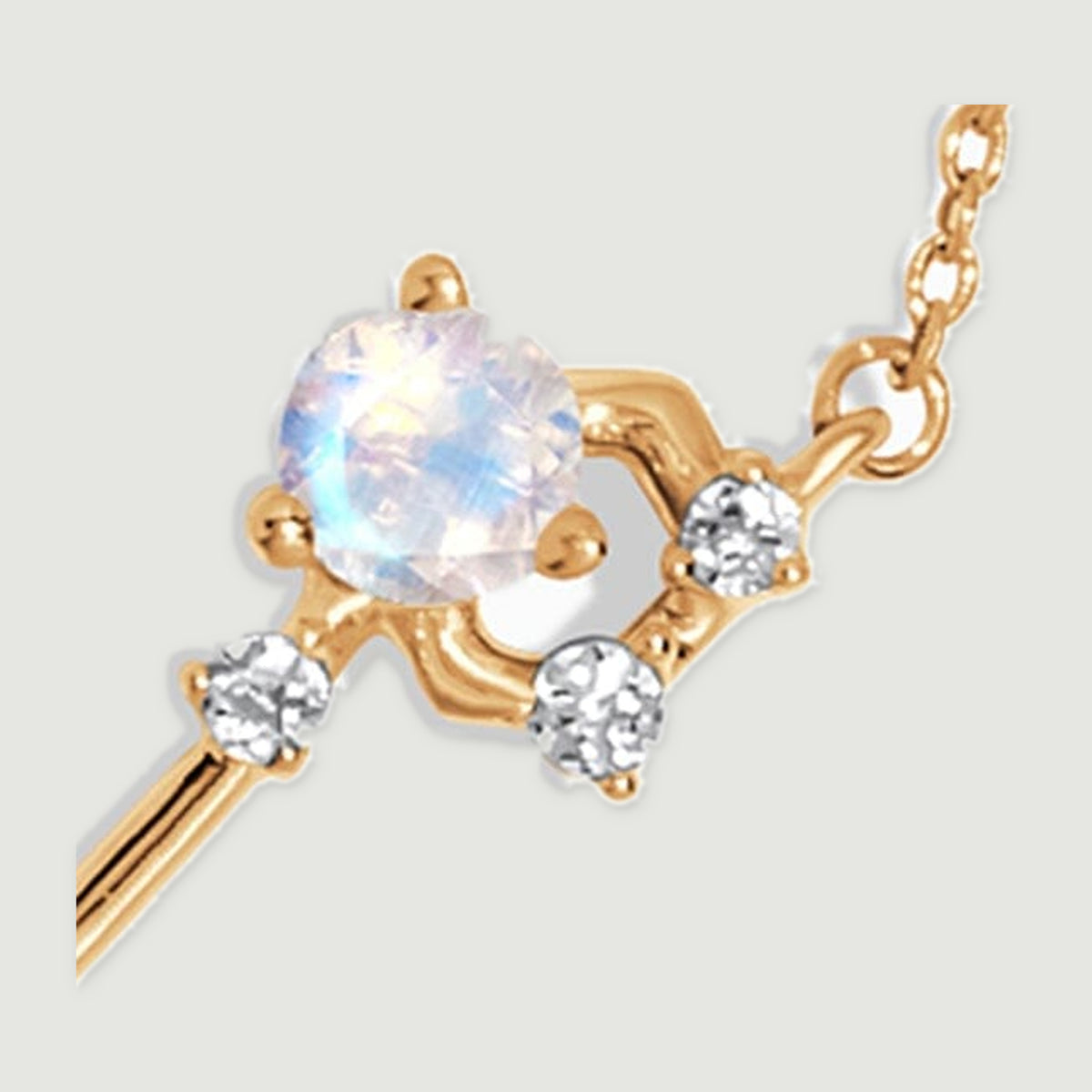 A large pale round stone sits beside smaller clear accents and polished yellow gold connectors.