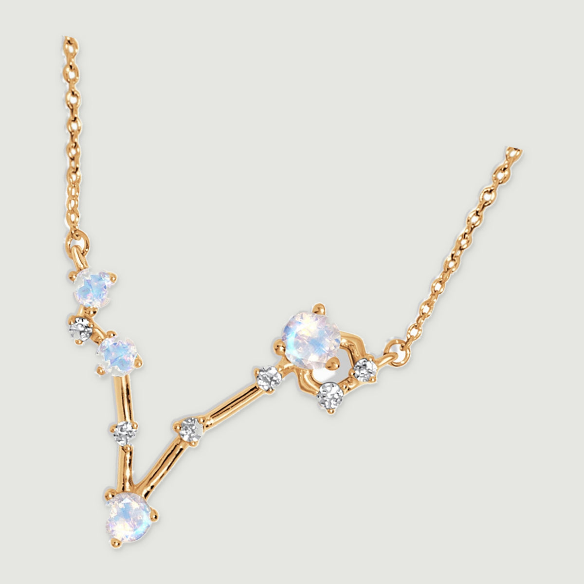 A yellow gold necklace lies diagonally on a light gray surface, showing the fine chain links and open V-shaped pendant.