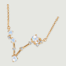 A yellow gold necklace lies diagonally on a light gray surface, showing the fine chain links and open V-shaped pendant.