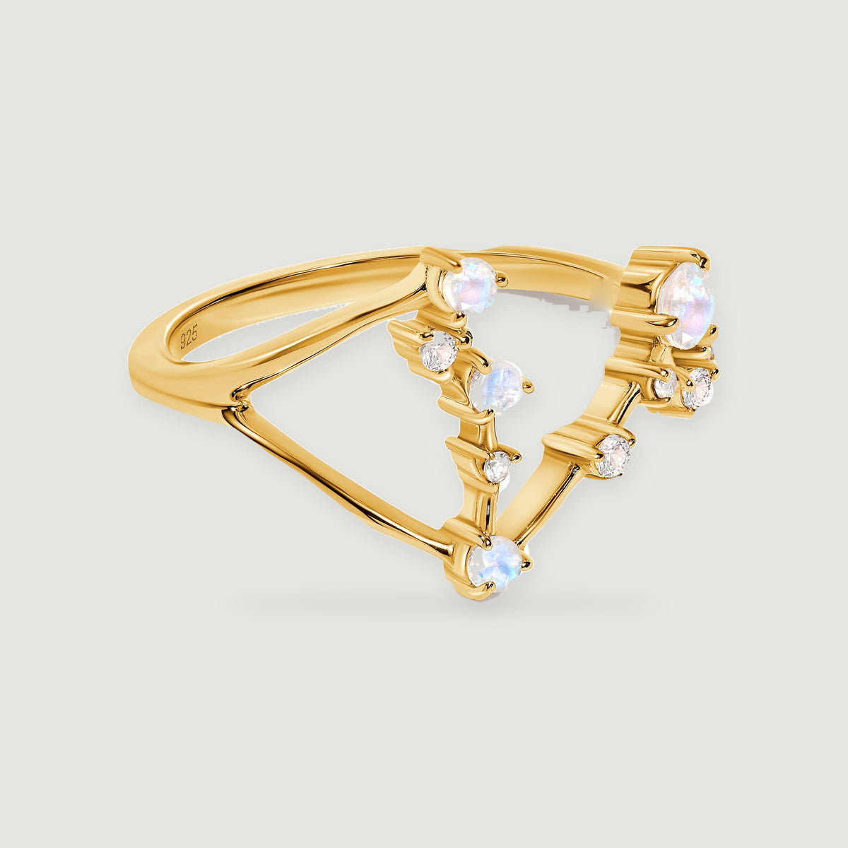 A yellow gold vermeil ring with round pale moonstones and small clear stones rests on a light gray surface.