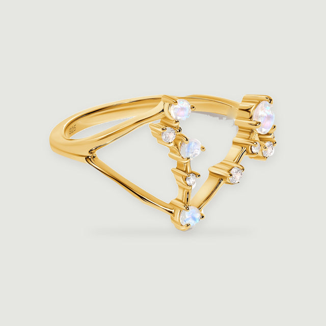 A yellow gold vermeil ring with round pale moonstones and small clear stones rests on a light gray surface.