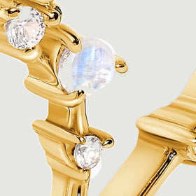 A close view shows pale round moonstones, clear accent stones, and polished yellow gold prongs.