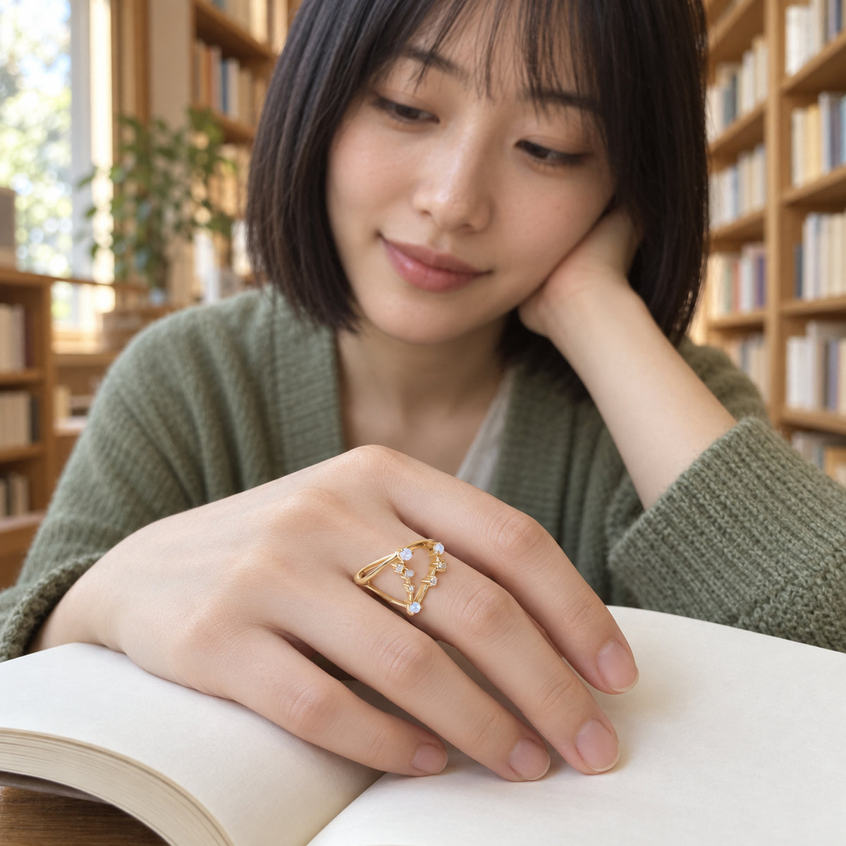 A woman with red hair wears the yellow gold moonstone ring on a freckled hand resting on a stone wall above the blue sea.