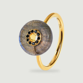 A yellow gold vermeil ring stands upright with a round grey labradorite disc and a circle of black stones at its centre.