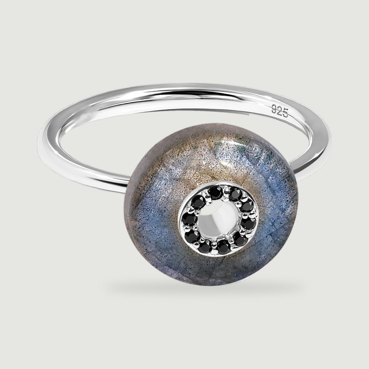A sterling silver ring rests diagonally with a blue-grey labradorite disc and black stones bordering the central opening.