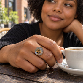 A yellow gold vermeil labradorite ring is worn on a hand beside a ceramic coffee cup on a wooden cafe table.