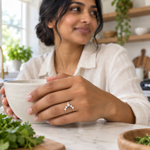 A white gold diamond ring is worn on a hand holding a ceramic bowl at a bright kitchen counter.