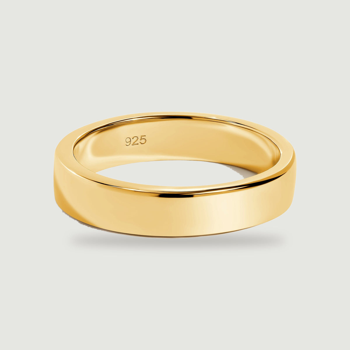 A polished yellow gold band is centered on a pale grey surface with a soft contact shadow.