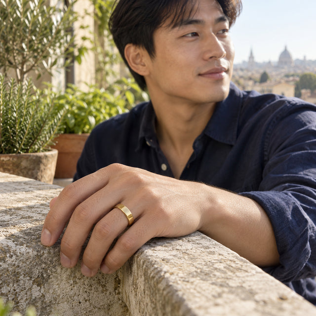 A man wears a smooth yellow gold band while resting his hand on a stone balcony railing.