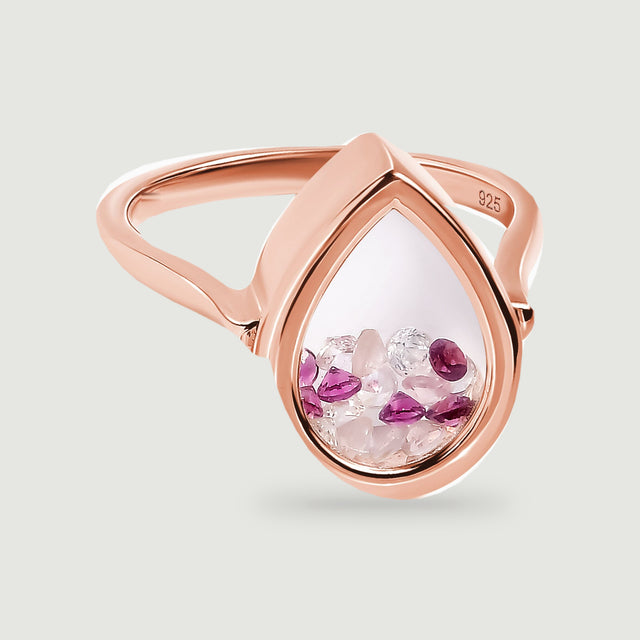 A rose gold vermeil ring is centered above a soft shadow with its pink and raspberry stones visible through the teardrop window.