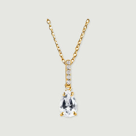 A yellow gold vermeil chain holds a faceted clear teardrop pendant beneath a sparkling bail on a light gray surface.