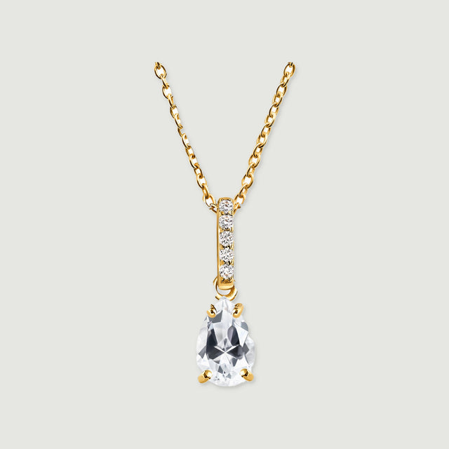 A yellow gold vermeil chain holds a faceted clear teardrop pendant beneath a sparkling bail on a light gray surface.