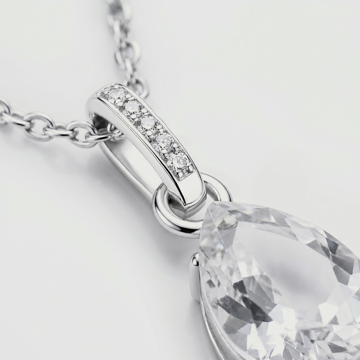 A close view shows the polished silver bail, its row of clear stones, and the upper facets of the pear-shaped pendant.