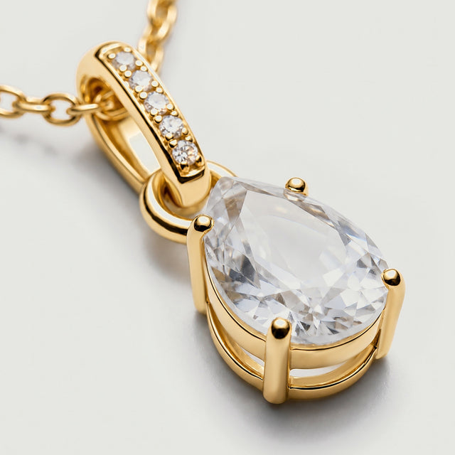 An angled close-up reveals the yellow gold vermeil prongs and open basket beneath the clear pear-shaped stone.