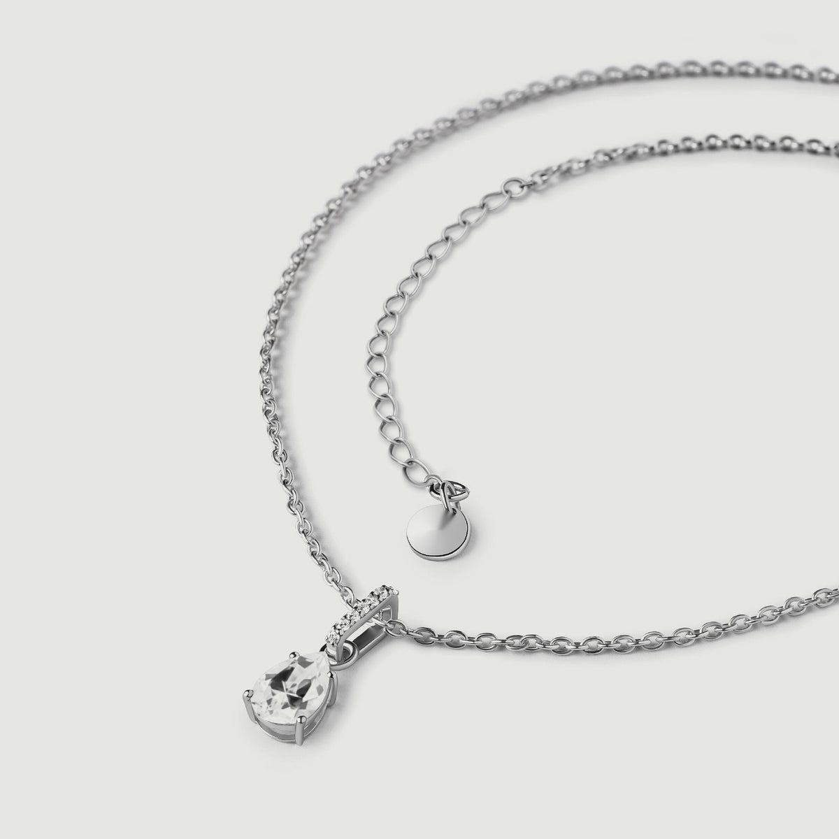 The sterling silver necklace lies in a loose curve with its clear pendant, extension links, and plain round end tag visible.