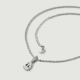The sterling silver necklace lies in a loose curve with its clear pendant, extension links, and plain round end tag visible.