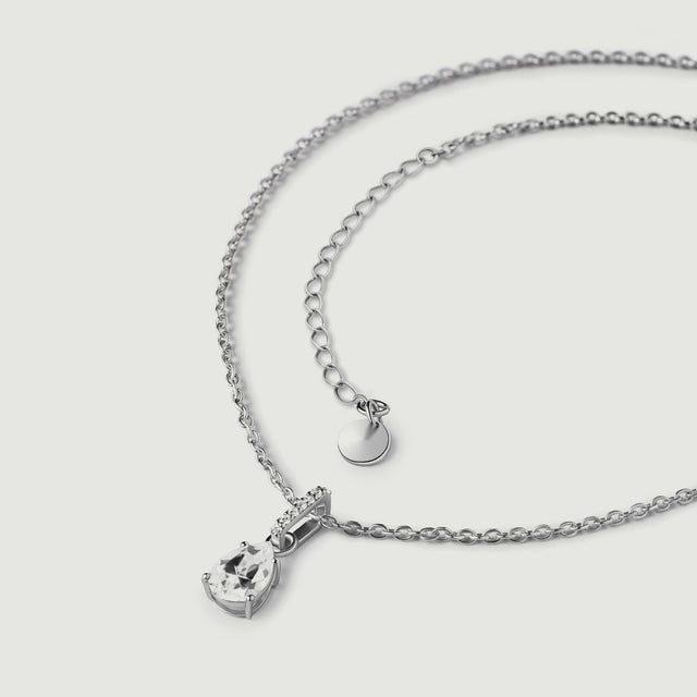 The sterling silver necklace lies in a loose curve with its clear pendant, extension links, and plain round end tag visible.