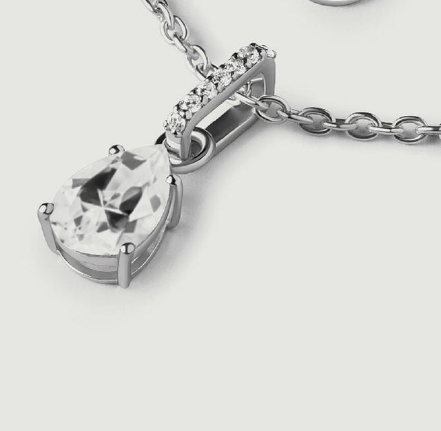 An oblique view of the silver pendant shows the pear-cut stone, curved bail, and raised side of the setting.