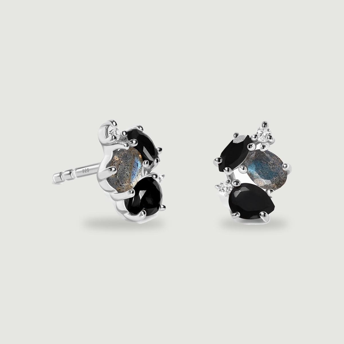 A pair of sterling silver cluster studs shows black faceted stones, blue grey labradorite and small clear accents on a light grey surface.