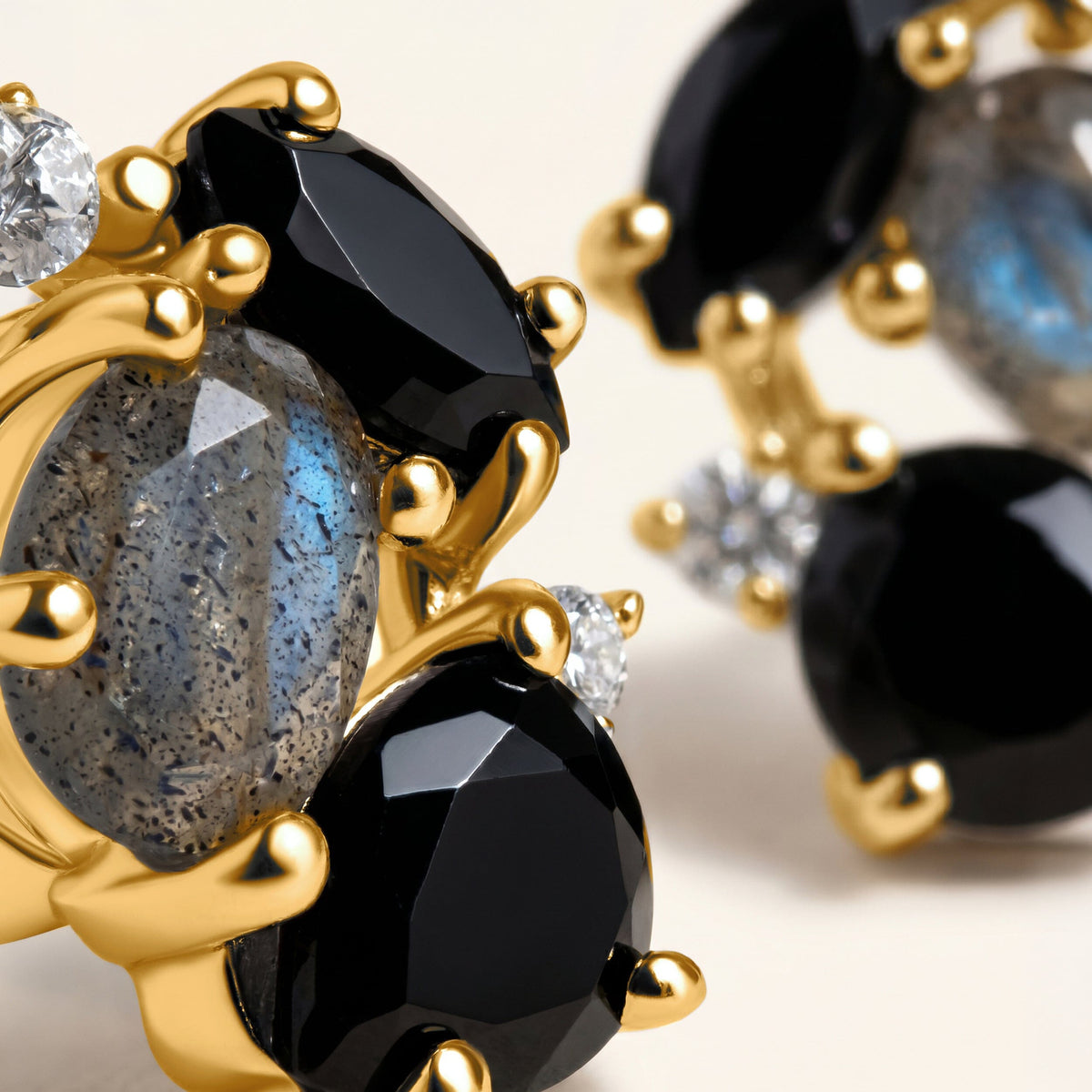 Golden rounded prongs frame black obsidian and grey blue labradorite while the second earring falls softly out of focus.