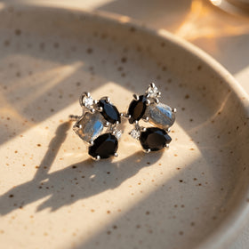 Two silver cluster earrings rest on a speckled ceramic dish crossed by warm sunlight and natural shadows.