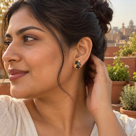 A gold vermeil cluster stud is visible below a woman's dark bun as she tucks her hair back on a terrace.