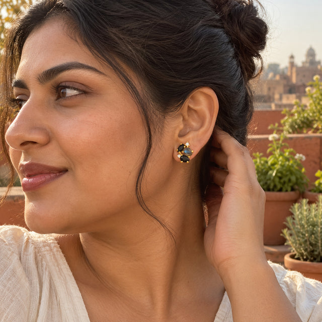 A gold vermeil cluster stud is visible below a woman's dark bun as she tucks her hair back on a terrace.