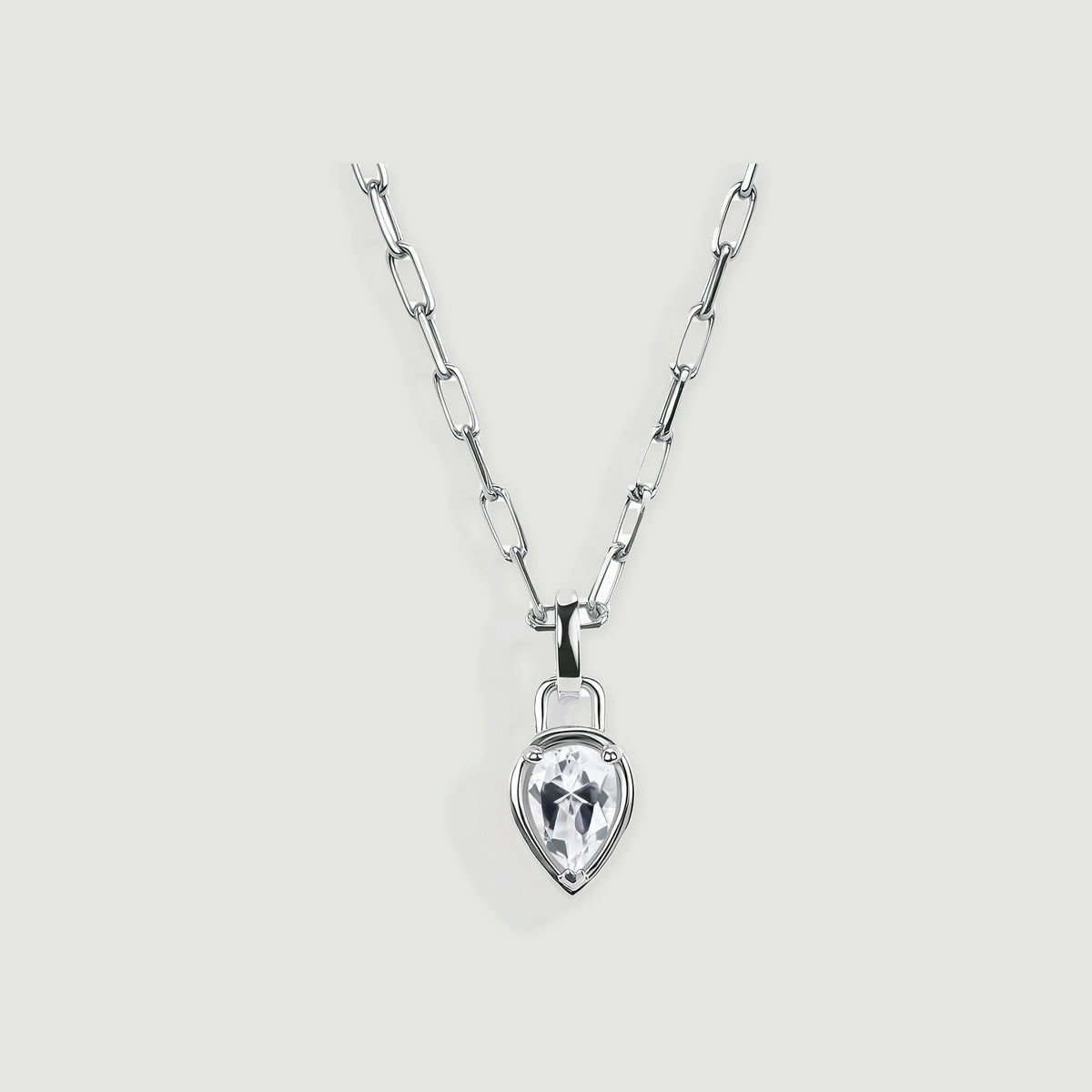 A silver-tone necklace with elongated links and a clear pear-shaped pendant is centered on a light gray surface.