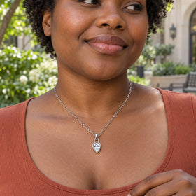 A woman with short curly hair wears a silver-tone link necklace over a terracotta top in a leafy courtyard.