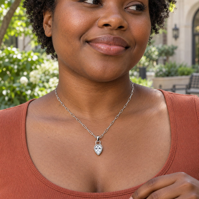 A woman with short curly hair wears a silver-tone link necklace over a terracotta top in a leafy courtyard.
