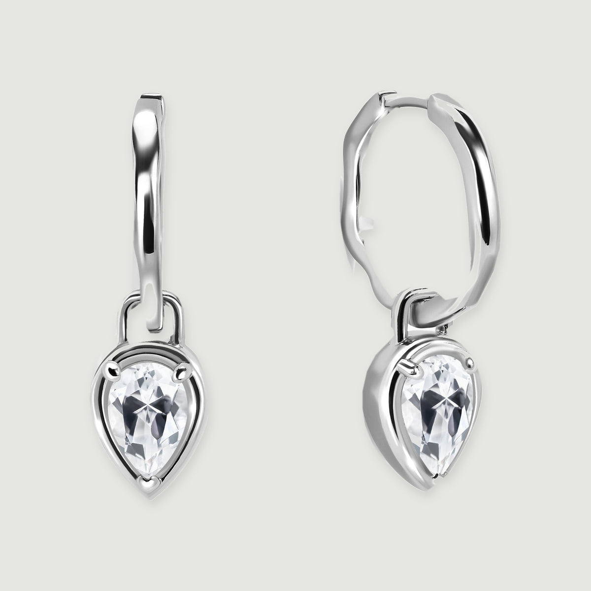 A pair of silver-toned hoop earrings with pear-shaped clear stones rests on a light gray background.