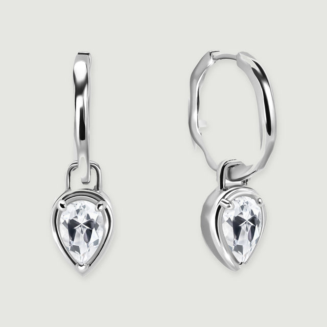 A pair of silver-toned hoop earrings with pear-shaped clear stones rests on a light gray background.