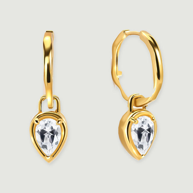 A pair of yellow-gold hoop earrings with pear-shaped clear stones rests on a light gray background.