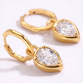 The foreground earring shows a pear-shaped clear stone in a yellow-gold setting with a second hoop behind it.