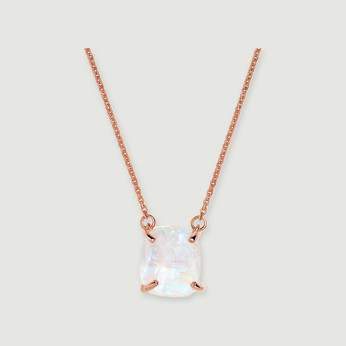 A raw white moonstone pendant with four rose gold prongs hangs from a fine link chain on a pale grey background.