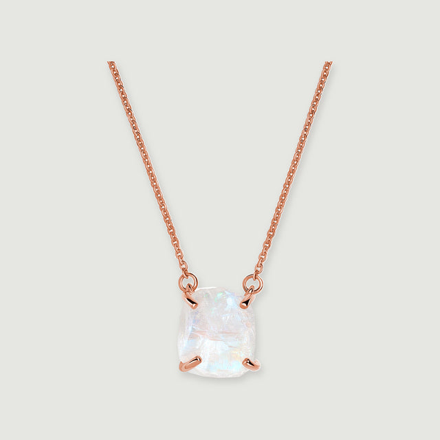 A raw white moonstone pendant with four rose gold prongs hangs from a fine link chain on a pale grey background.