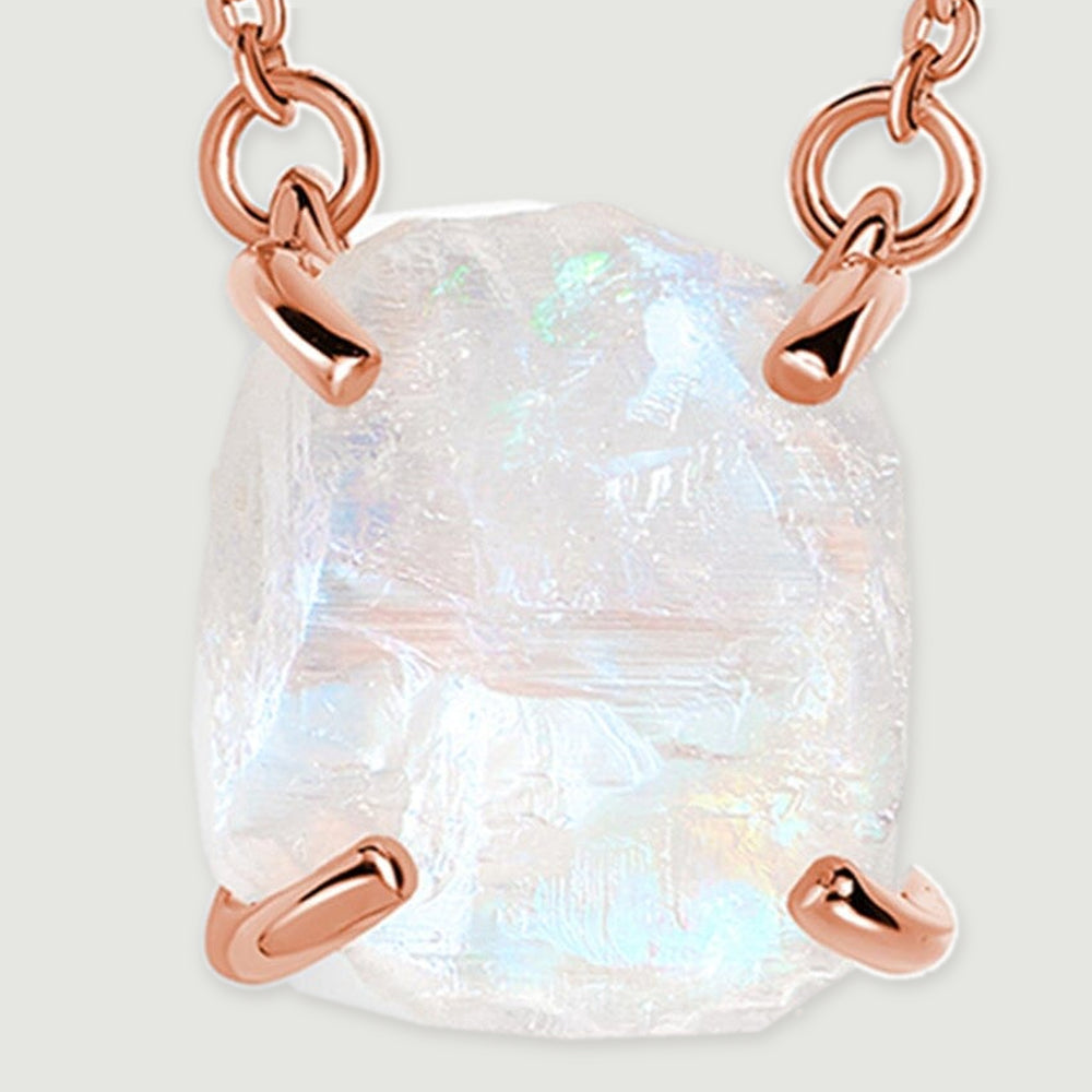 Blue flashes and uneven ridges are visible across the raw moonstone held by rose gold corner prongs.