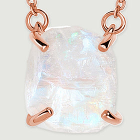 Blue flashes and uneven ridges are visible across the raw moonstone held by rose gold corner prongs.