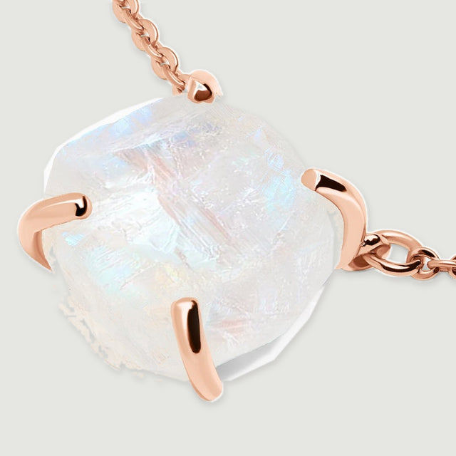 An angled view shows the raised raw moonstone and curved rose gold prongs with a short section of chain.