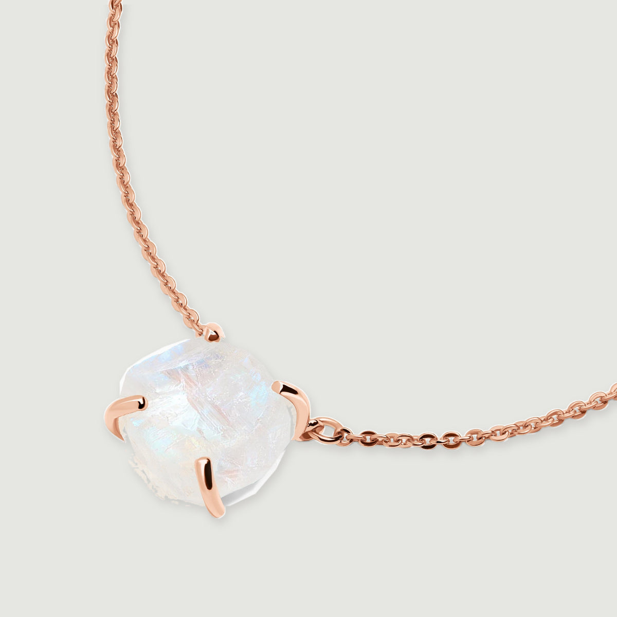 The rose gold necklace lies diagonally on a pale grey surface with the moonstone near the lower left.