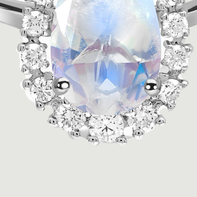 The lower moonstone facets display pale blue reflections beside the diamond halo and two rounded prongs.