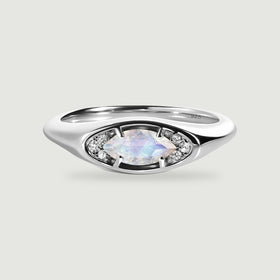 A polished silver ring frames a pale faceted moonstone between two clusters of small clear stones.