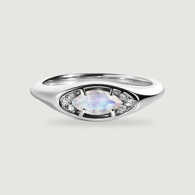 A polished silver ring frames a pale faceted moonstone between two clusters of small clear stones.