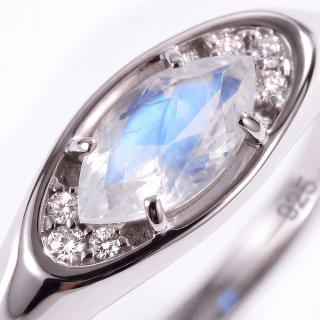 A close view of the silver setting shows four prongs around a blue-flashing moonstone and clear round accents.
