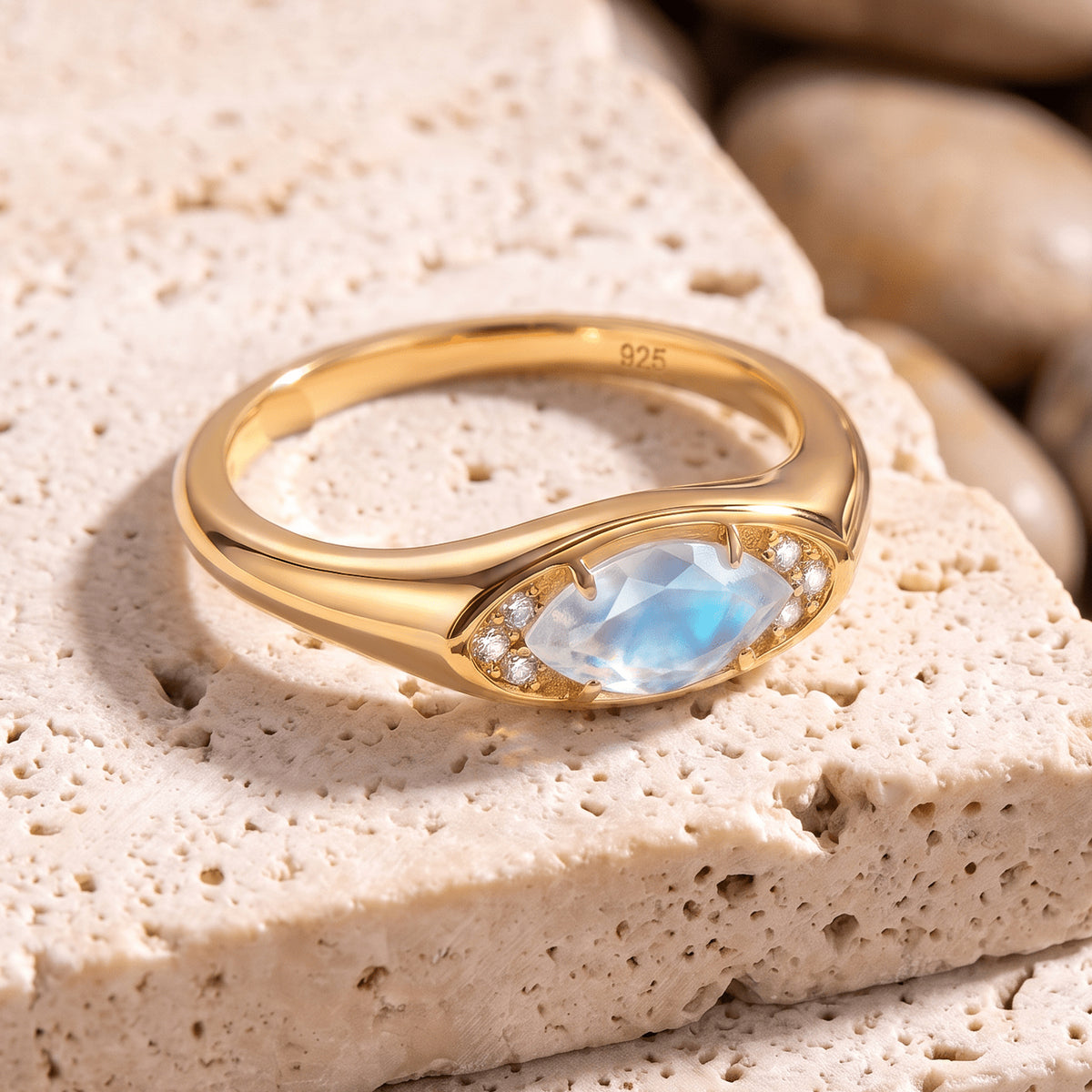 A yellow gold moonstone ring lies on pale travertine with its smooth band and raised setting visible.