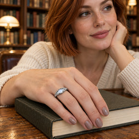 A woman with copper-colored hair wears the silver moonstone ring while resting her hand on a dark book.