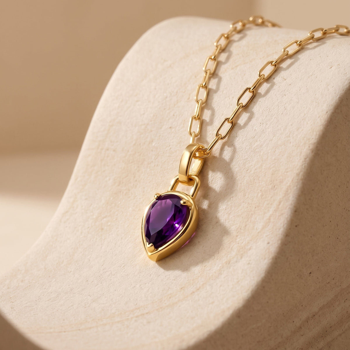 The gold-colored chain and purple pendant rest diagonally across a cream stone surface.