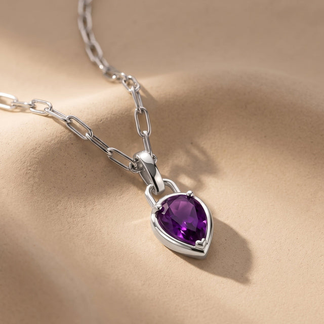 An elongated silver-colored link chain leads to a purple pendant lying on a textured beige surface.