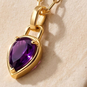 An angled close-up shows the raised gold-colored edge around a purple pear-shaped gemstone on cream stone.