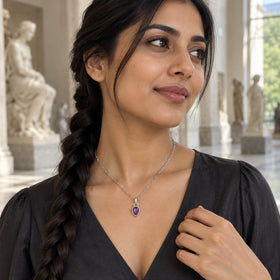 A woman with a long braid wears a silver-colored amethyst necklace with a charcoal blouse in a sculpture gallery.